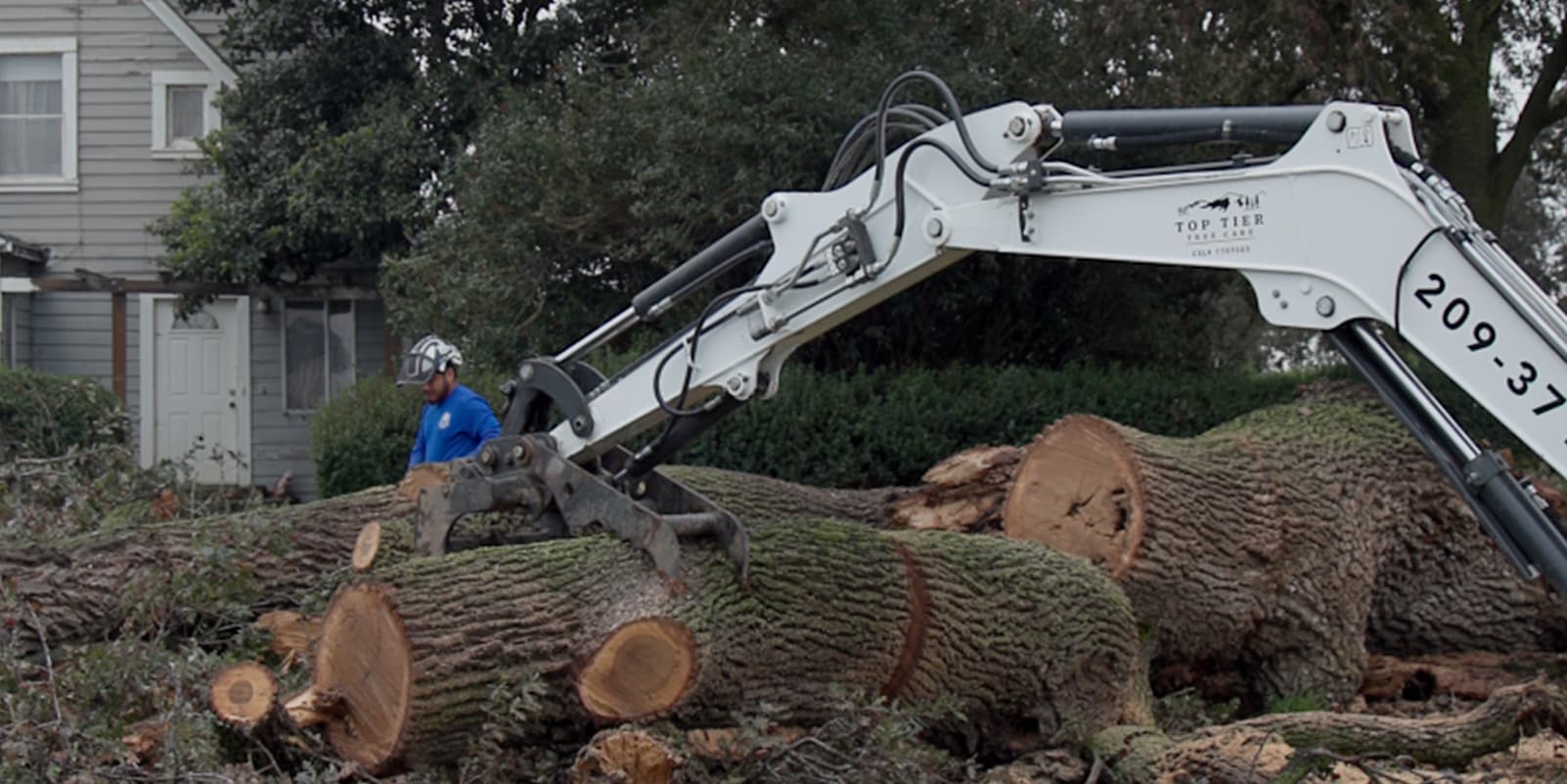 Top Tier grapple machine removing large tree logs from a yard